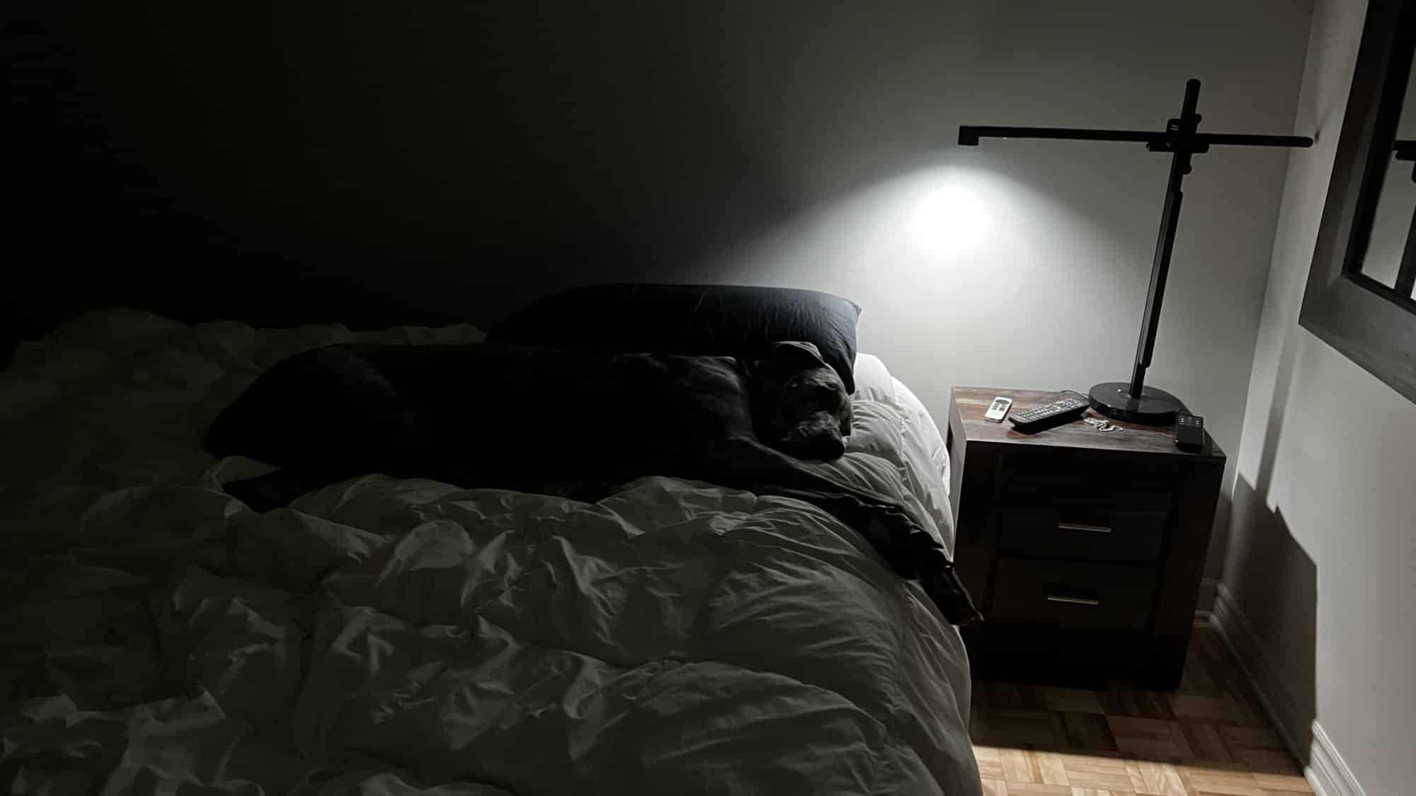 Une chambre dans la pénombre, une lampe allumée sur la table de chevet.