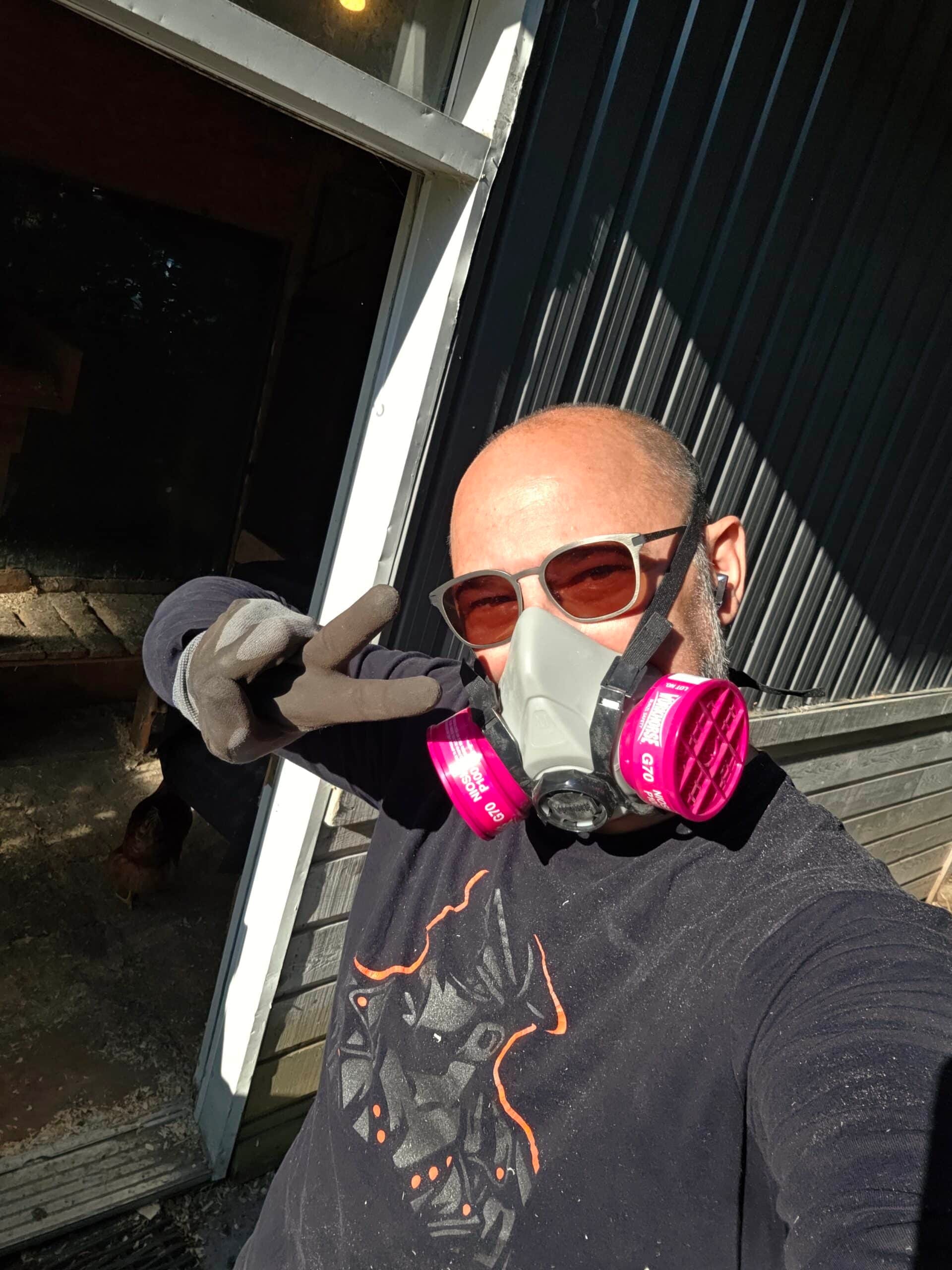 Un homme en masque respiratoire et gants, devant le poulailler.