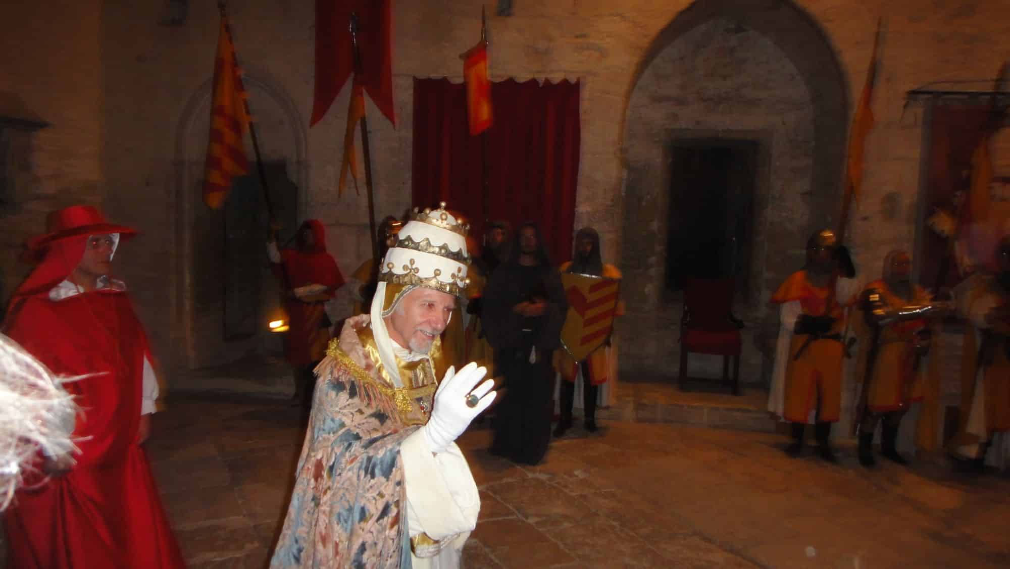 Un comédien costumé en pape salue devant les bannières.