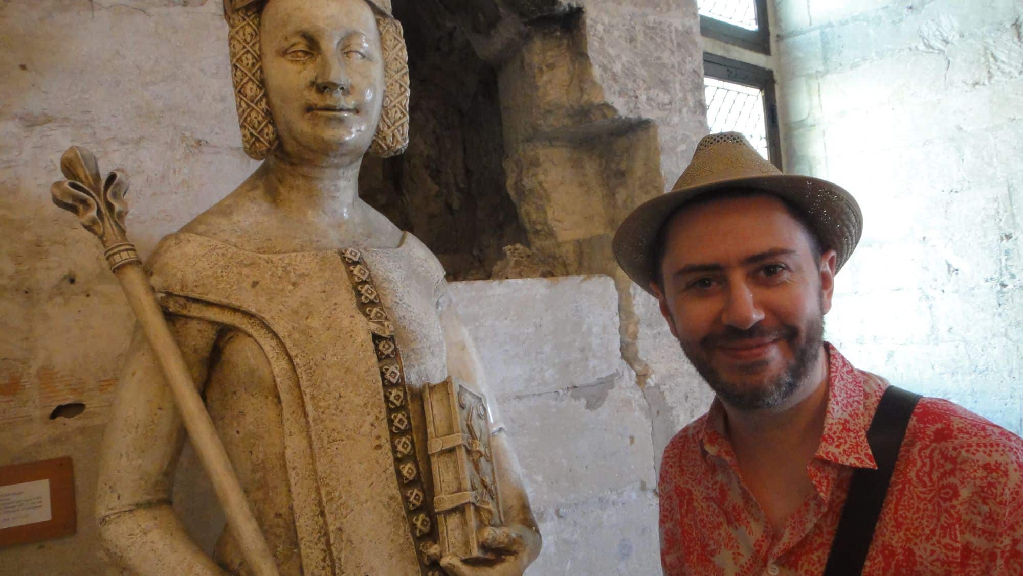Un homme pose à côté d'une statue de pierre sculptée.