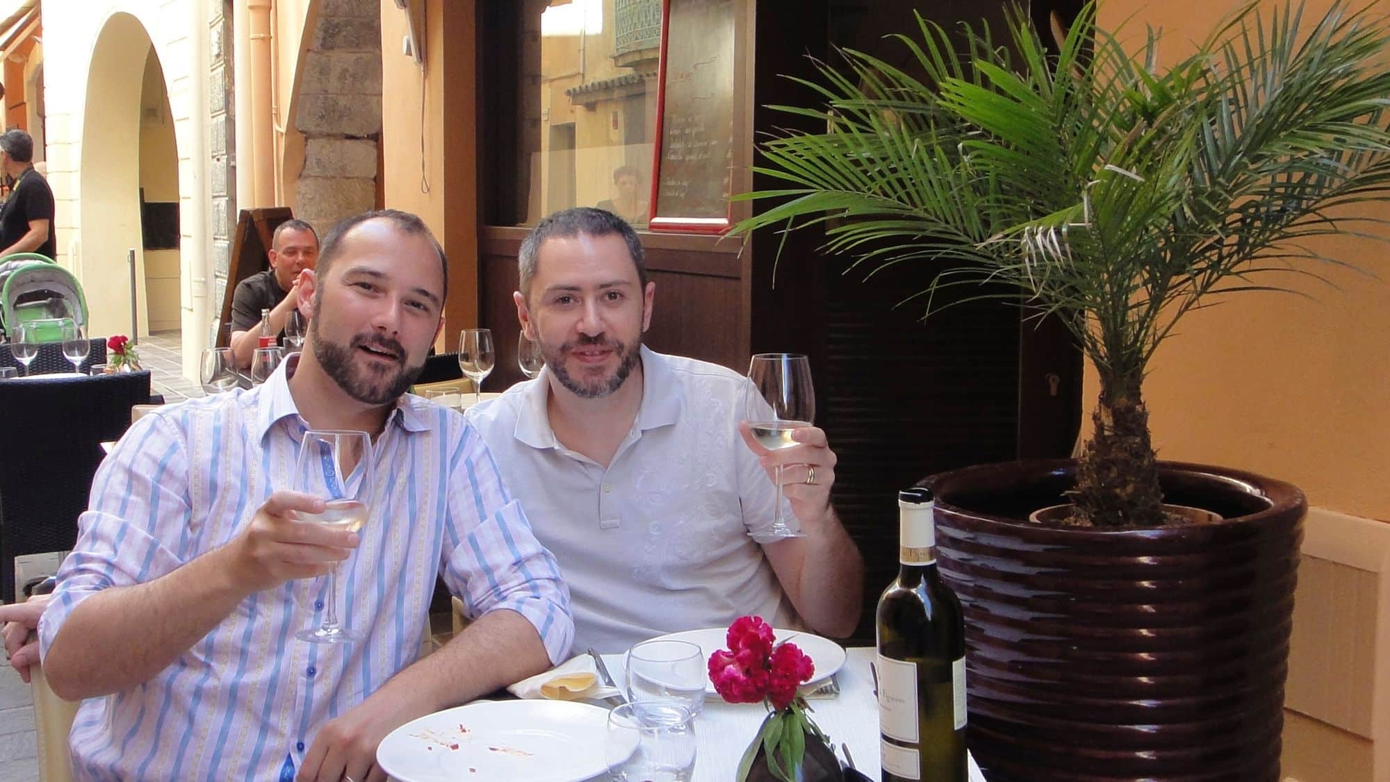 Deux hommes trinquent à la terrasse d'un restaurant.