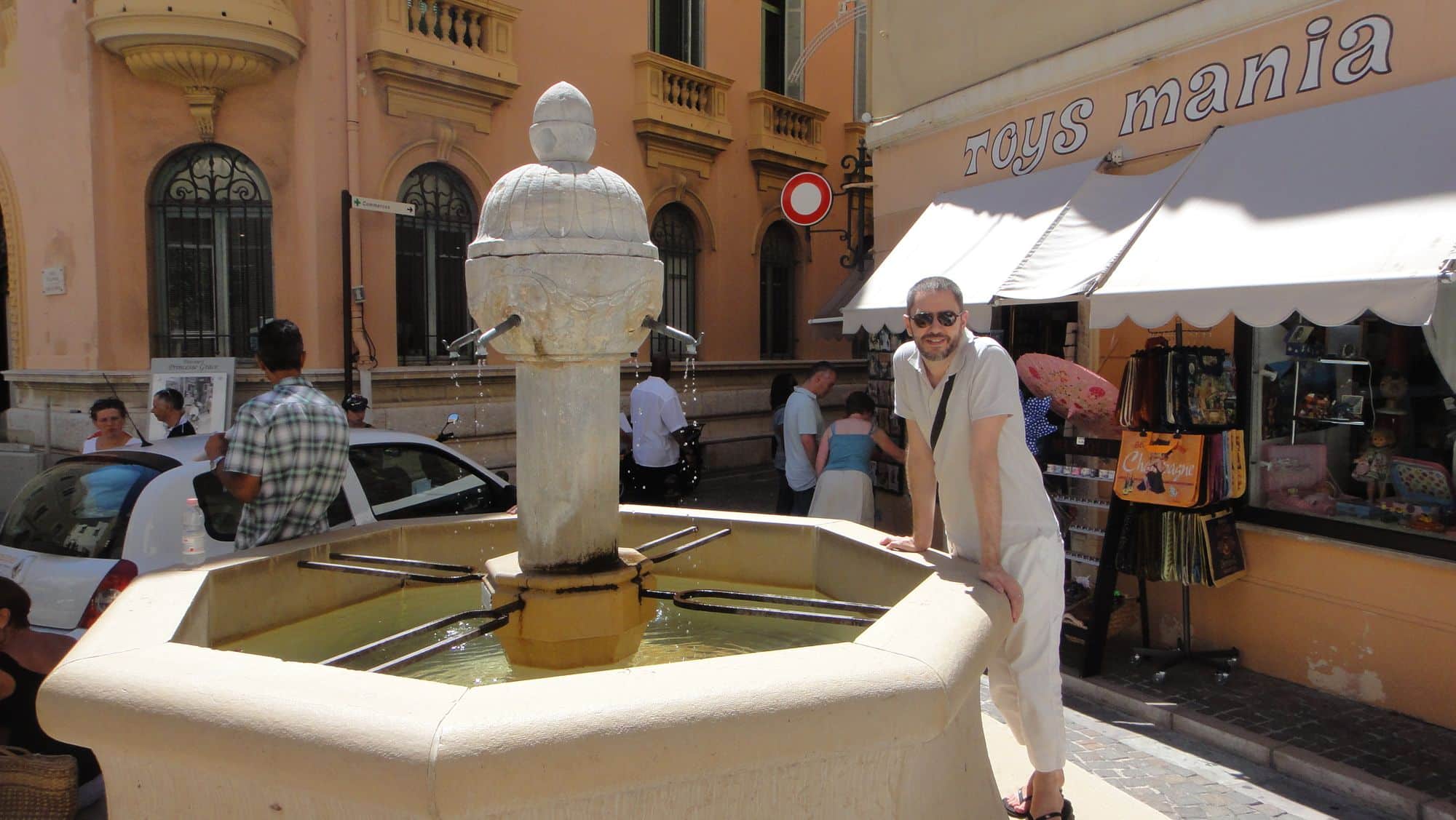 Une fontaine blanche au milieu d'une rue commerçante.