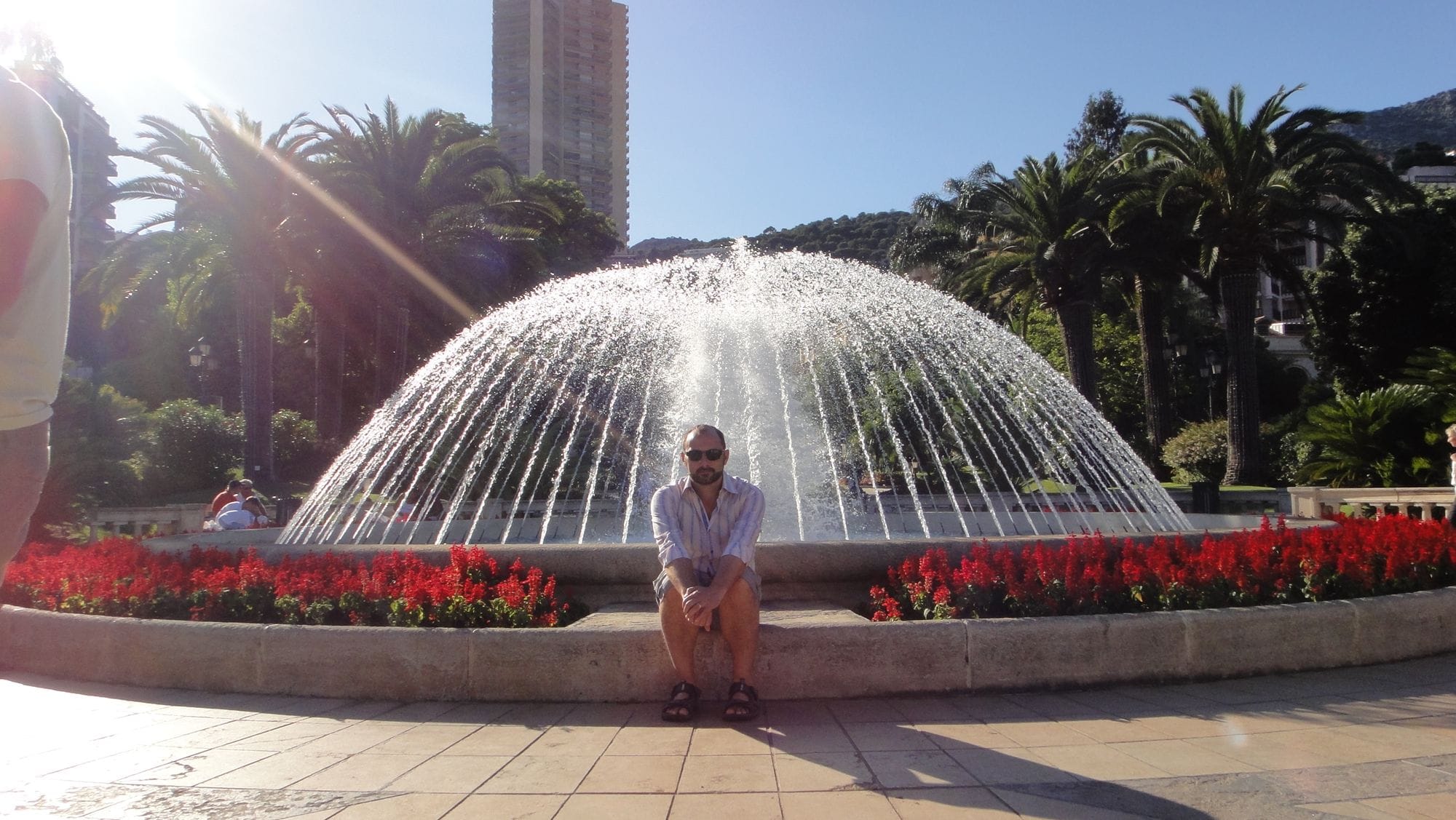 Assis au bord d'une grande fontaine, dans un jardin public.