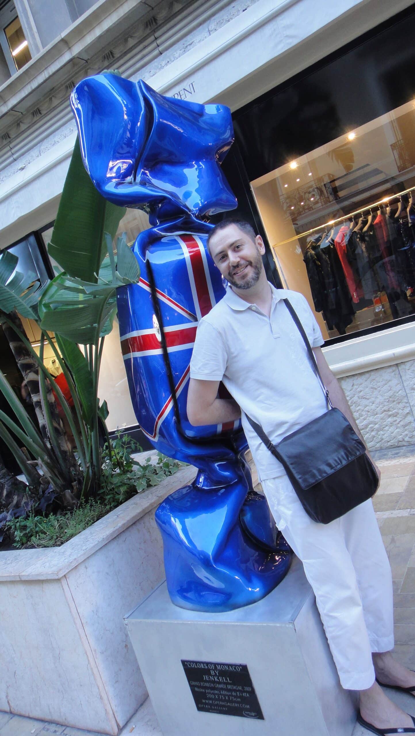 Un homme pose à côté d'une sculpture bleue, devant une boutique.