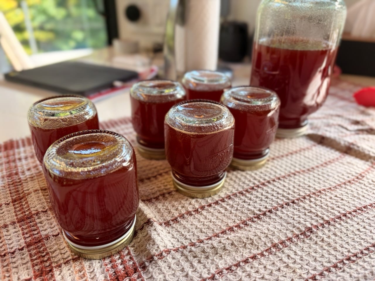 Six des pots de gelée de raisin, retournés sur un linge à carreaux, à côté du grand pot.