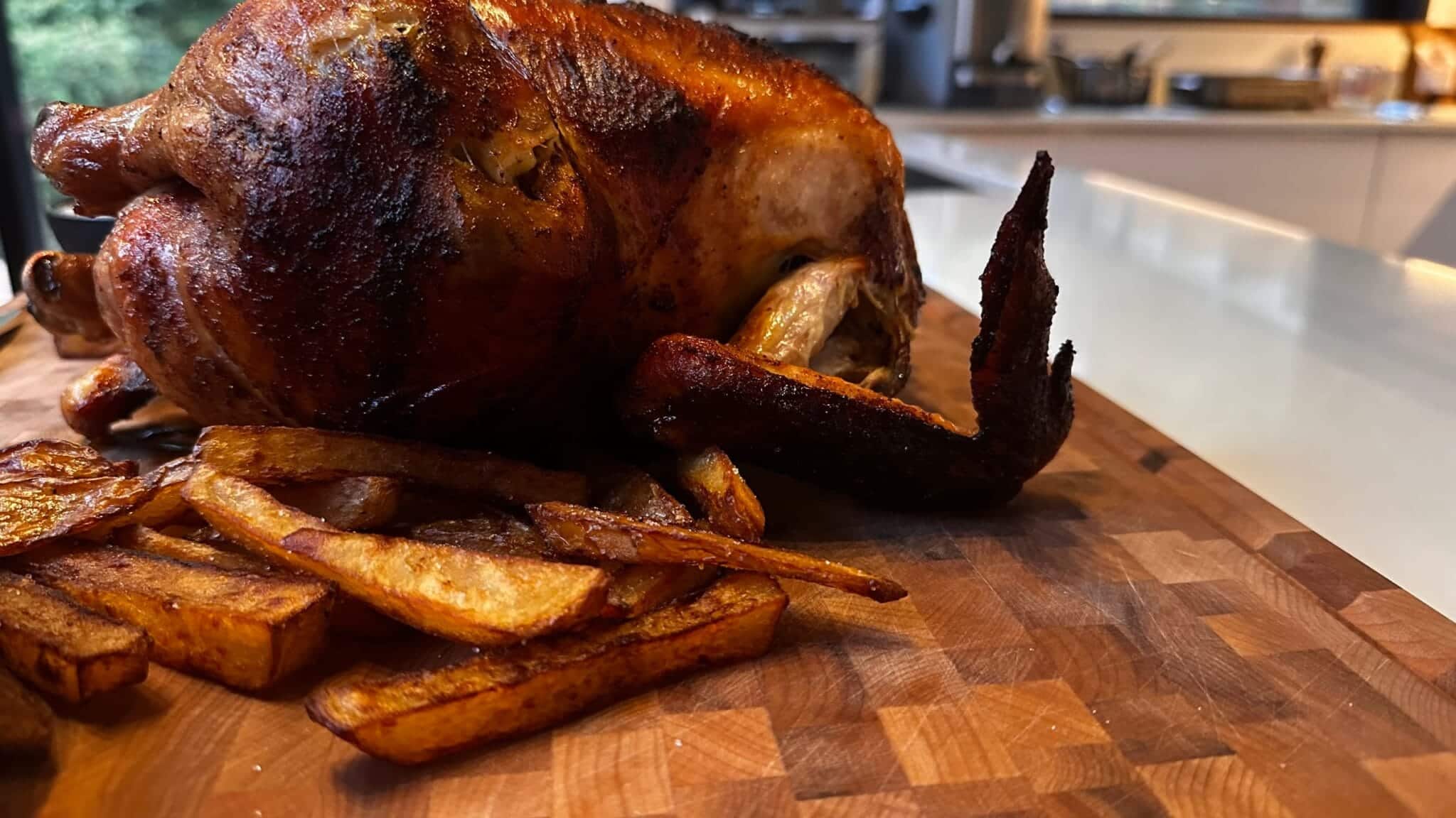 Un poulet rôti et des pommes de terre sur une planche de bois.