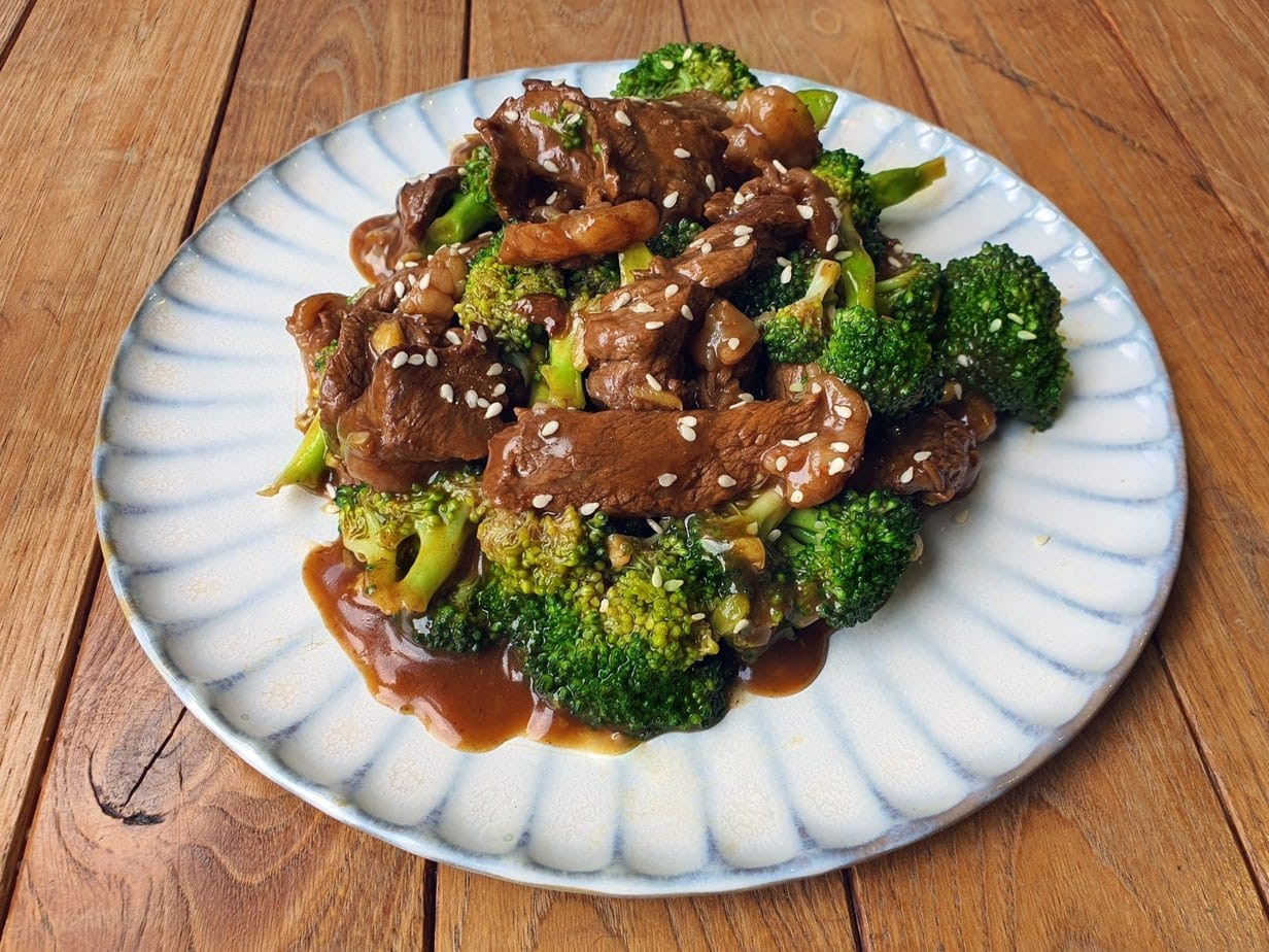 Un plat de bœuf au brocoli nappé de sauce, sur assiette blanche.