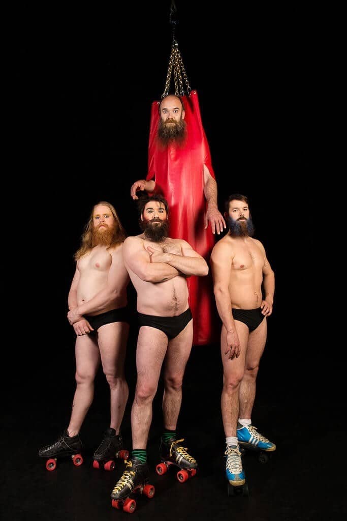 Quatre artistes barbus en patins à roulettes, l'un suspendu à un tissu rouge.
