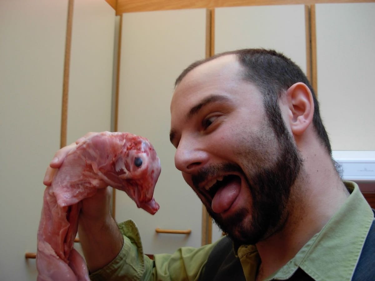 Un homme tient un lapin cru par les pattes, l'air taquin, dans la cuisine.