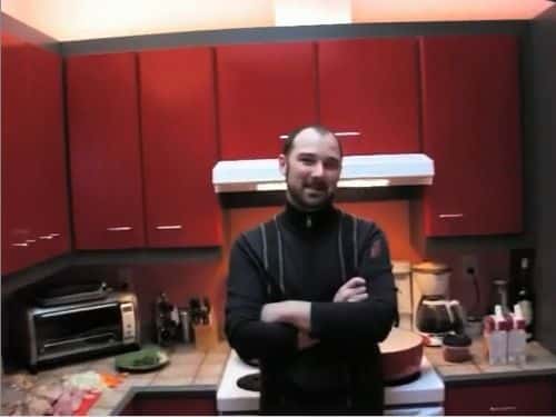 Un homme bras croisés dans sa cuisine rouge, avant la préparation du cassoulet.